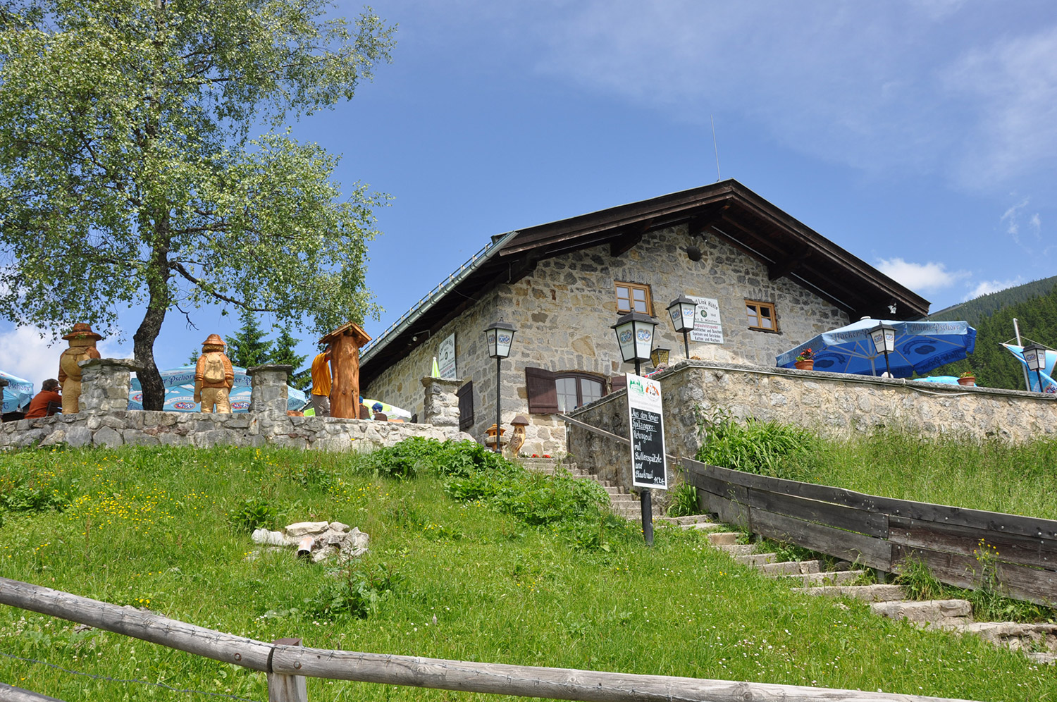 Bild Aufnahme der Albert-Link-Hütte auf einem sonnenbeschienenen, grünen Hügel.