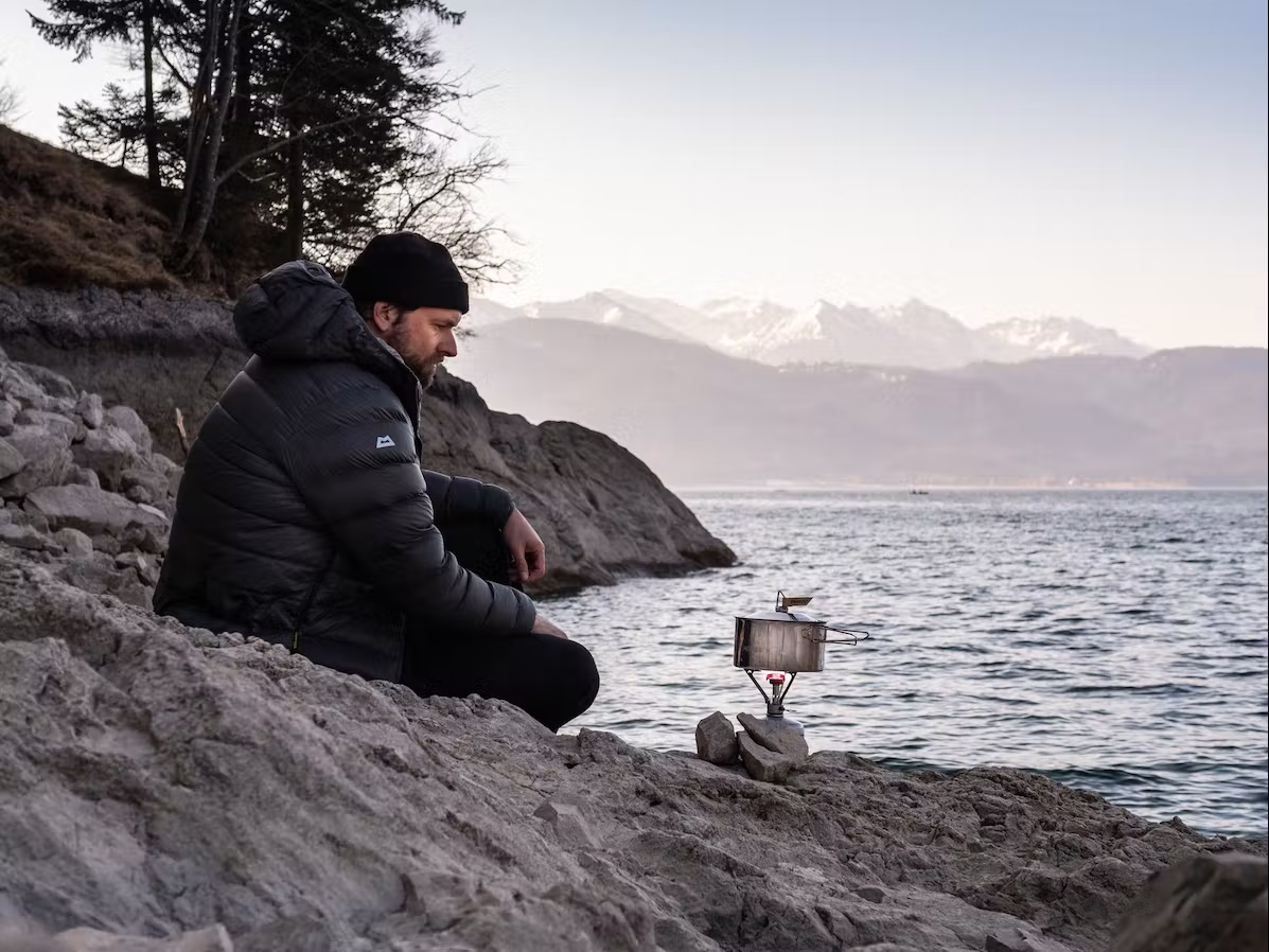 Bild Ein Mann sitzt am Wasser mit seinem Campingkocher