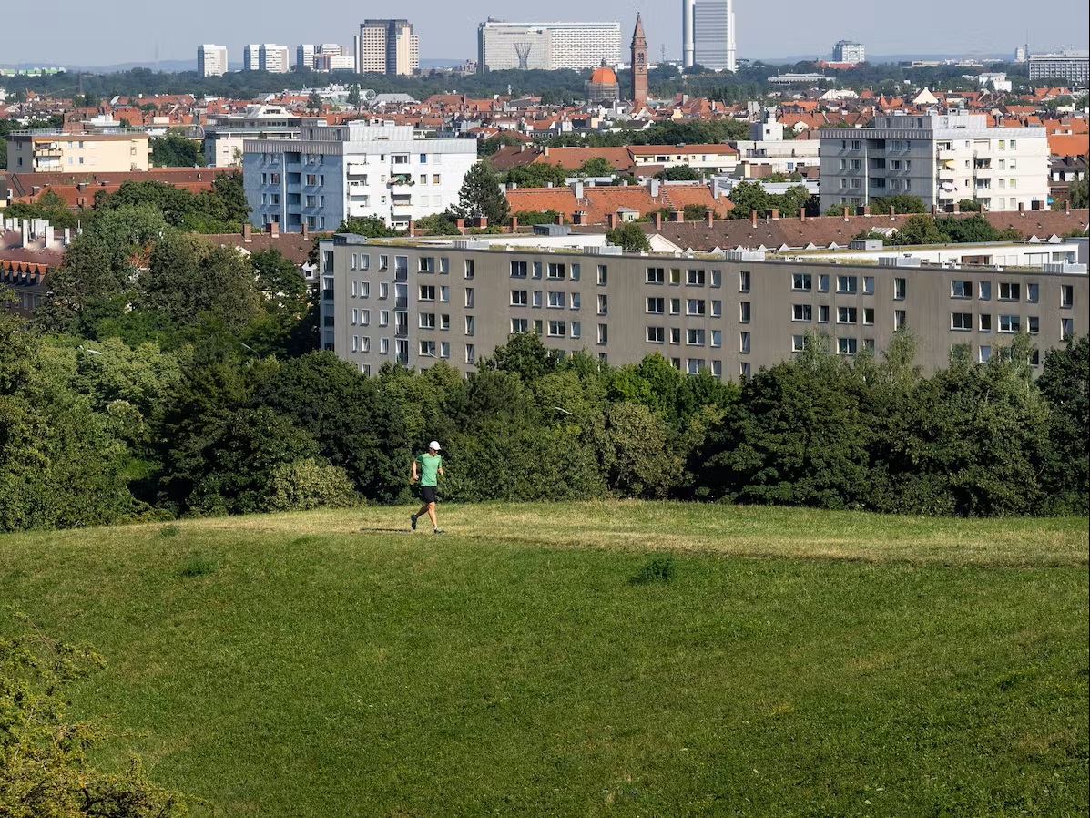 Bild Läufer läuft am Olympiaberg, im Hintergrund Stadt München und die Berge