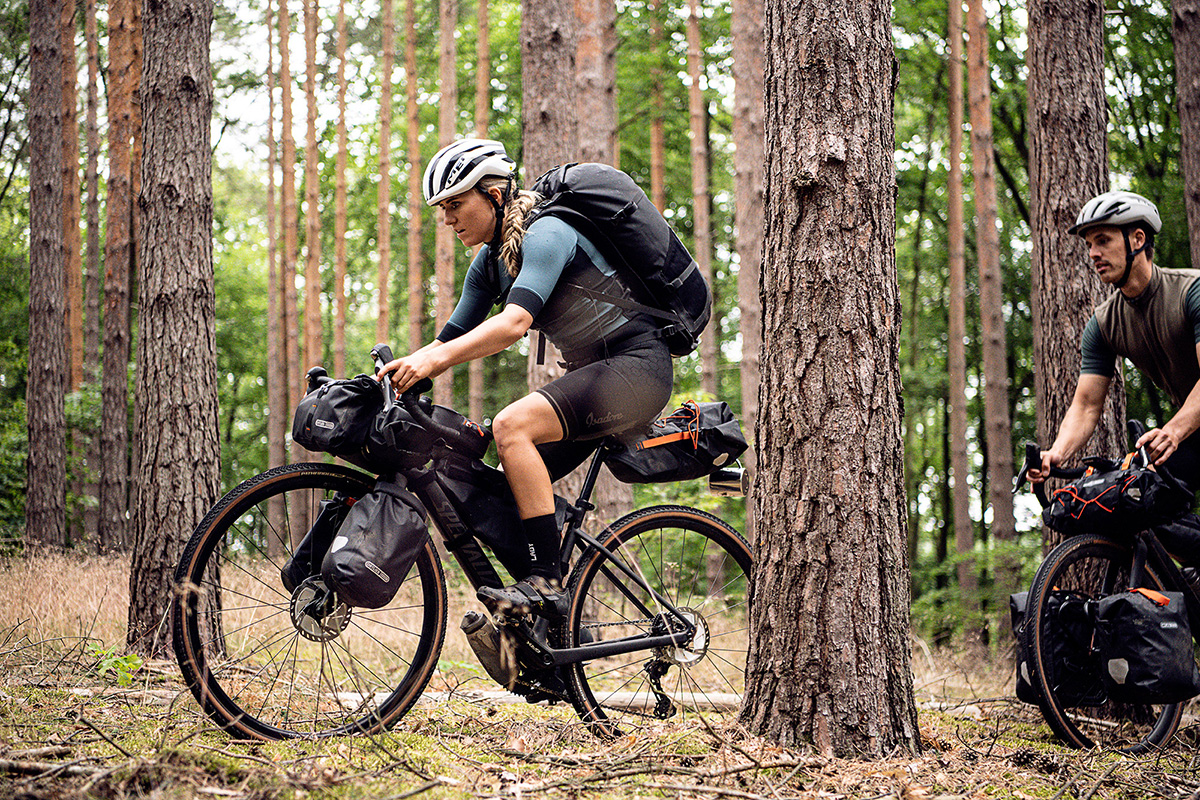 Bild Eine Frau und ein Mann fahren auf vollbepackten Fahrrädern durch einen Wald