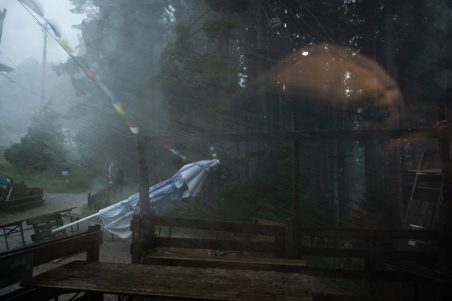 Bild Sturm und Regen auf dem Berg. Man sieht einen umgefallenen Schirm und Regenschwaden.
