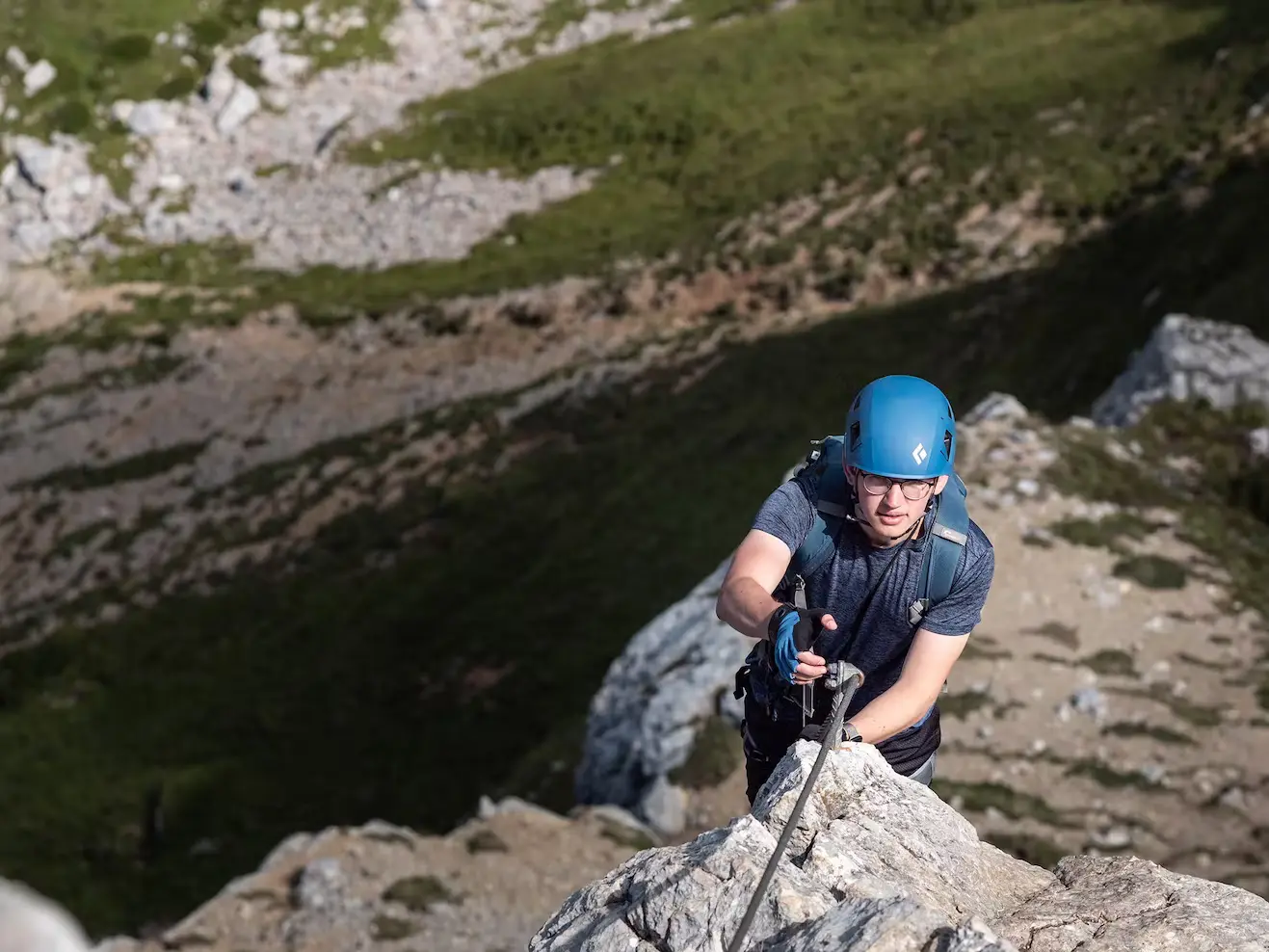 Bild Junger Mann mit blauem Helm steigt hoch über dem Boden durch einen steilen Klettersteig.