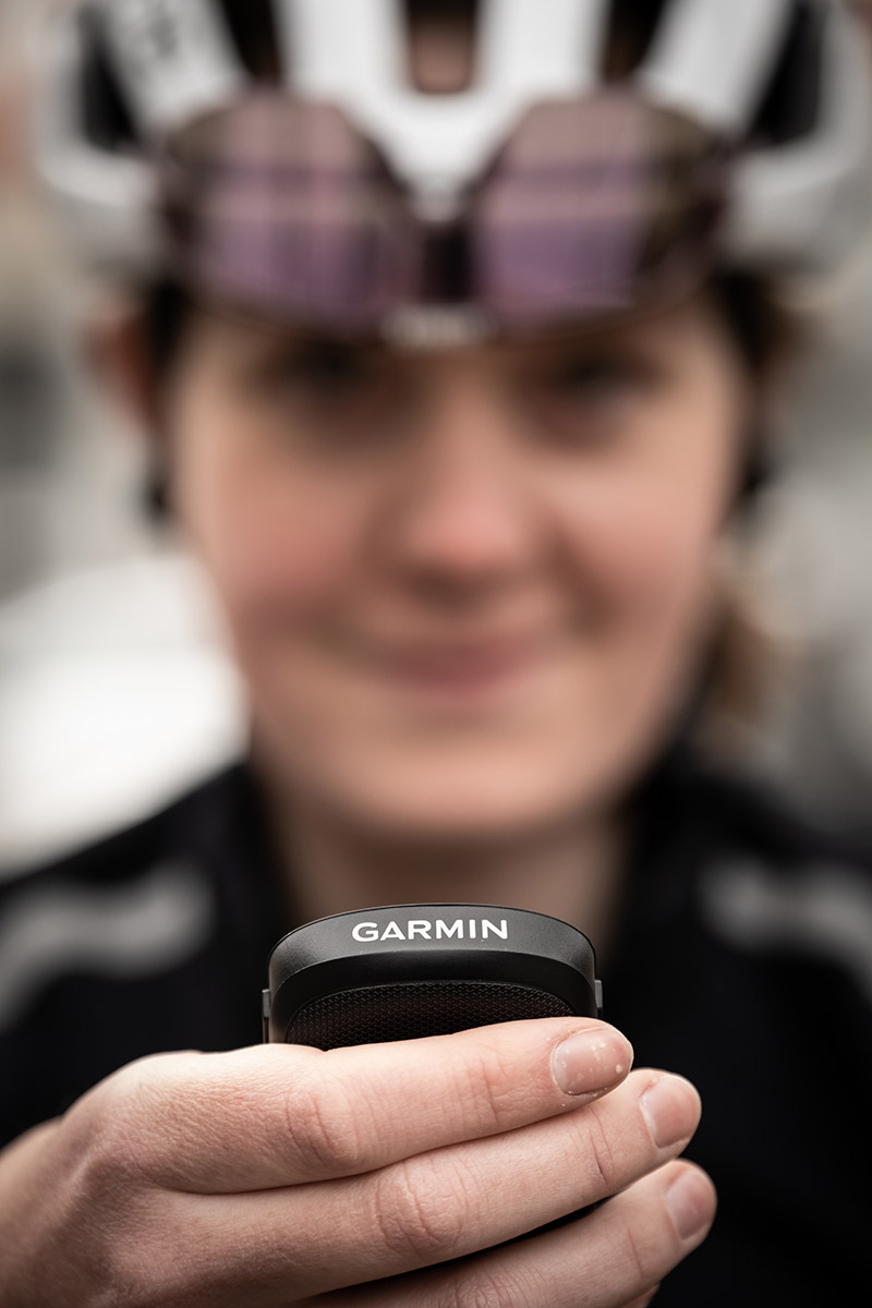 Bild Lächelnde Frau mit Fahrradhelm und Brille hält ein Garmin GPS Gerät in der Hand.