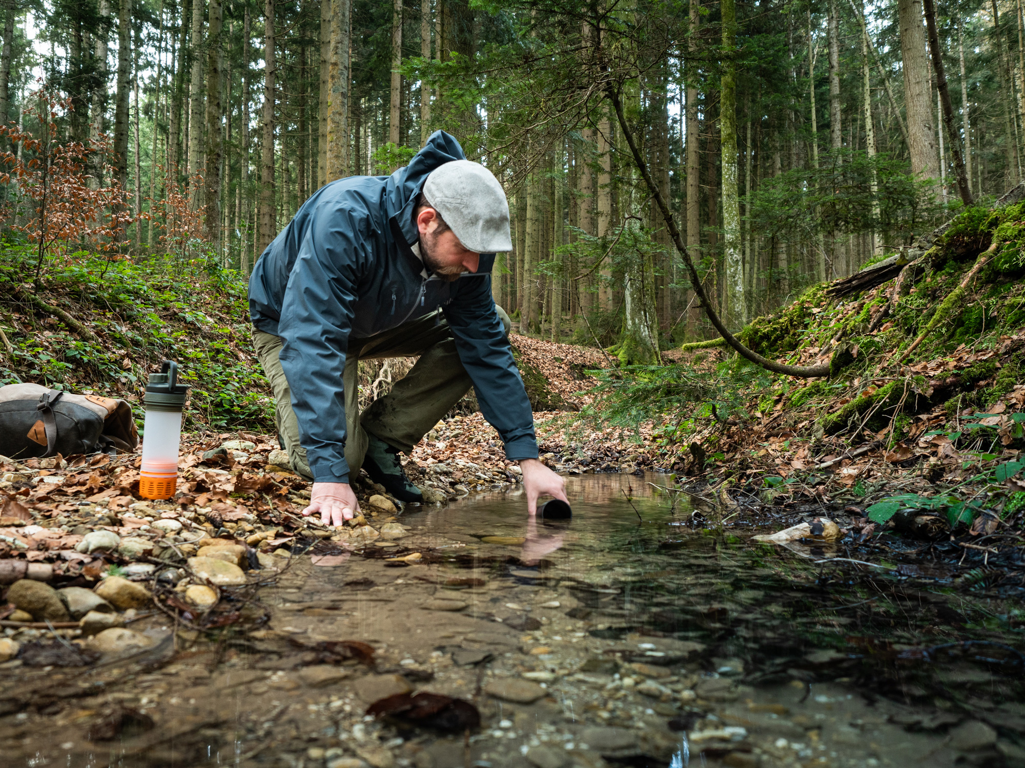 Bild Mann fuellt an einem Bach im Wald den Wasserfilter auf.