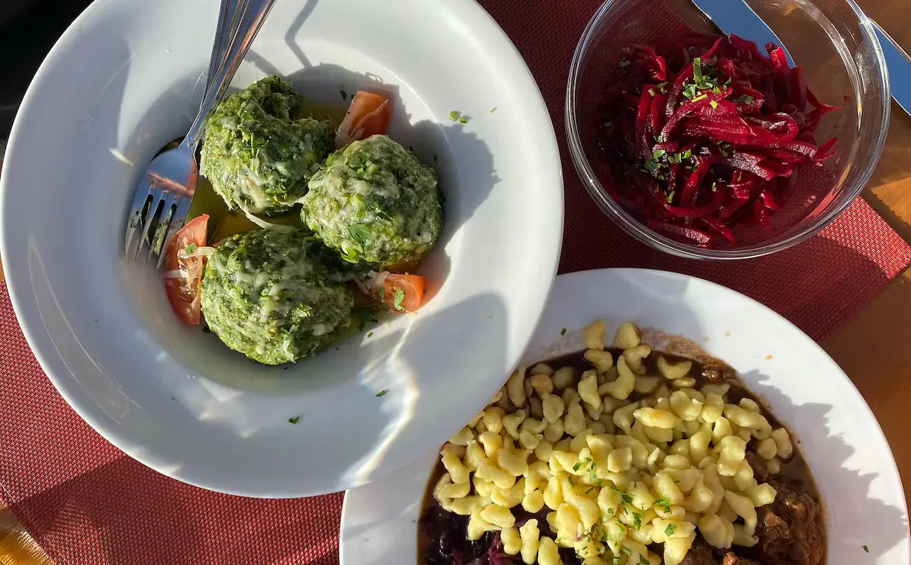 Bild Hüttenessen. In einem Teller liegen Spinatknödel, im anderen Spätzle.