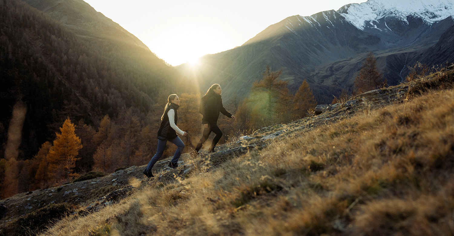 Bild Zwei Frauen wandern in einer alpinen Herbstlandschaft im Sonnenaufgang