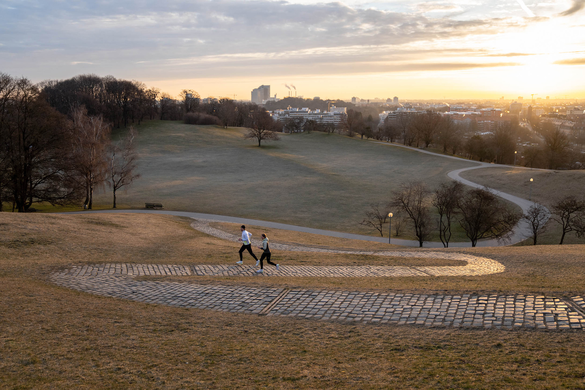 Zwei Läufer*innen bei Sonnenaufgang im Olympiapark