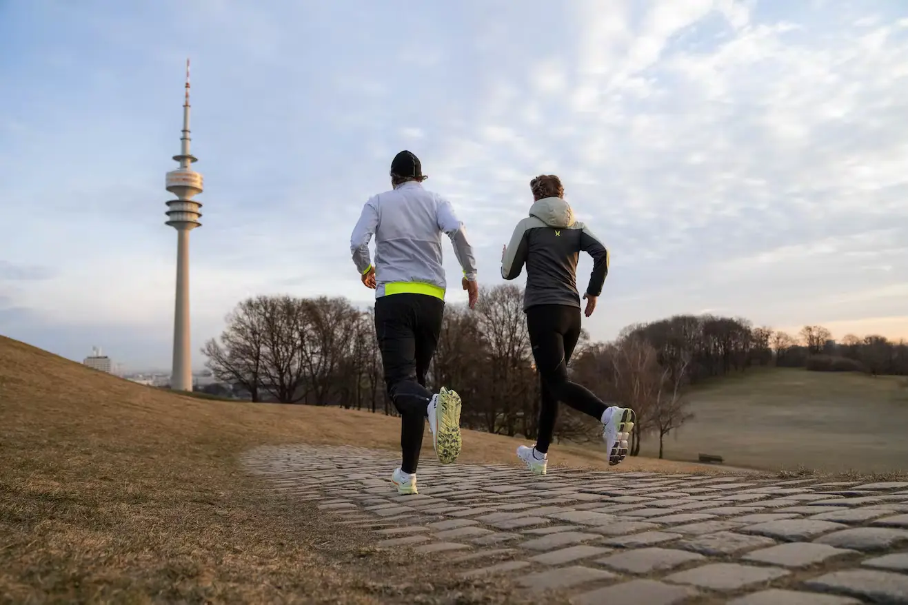 Bild 2 Läufer joggen im Olympiapark in München. Im Hintergrund der Olympiaturm.