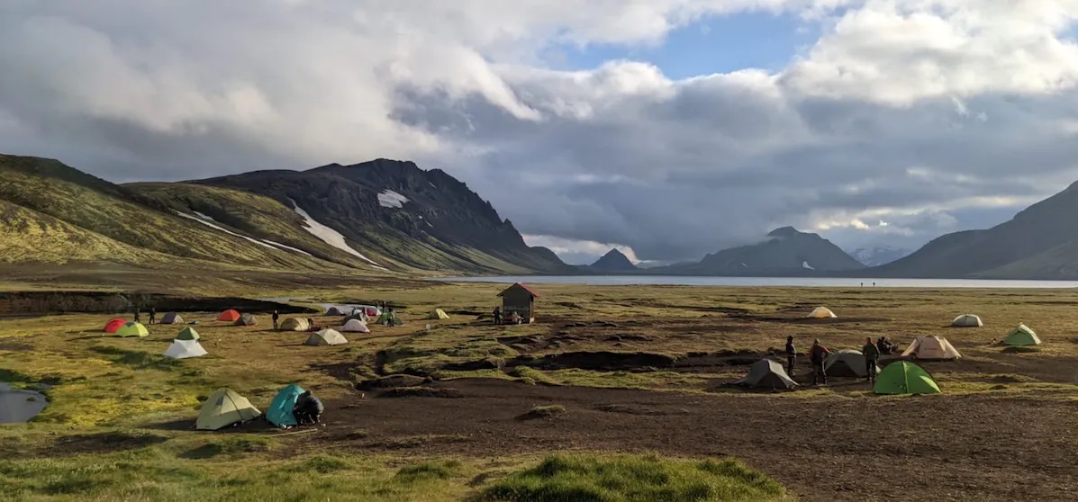 Bild Bild eines Campingplatzes am Ufer eines Sees in grüner Berglandschaft auf Island