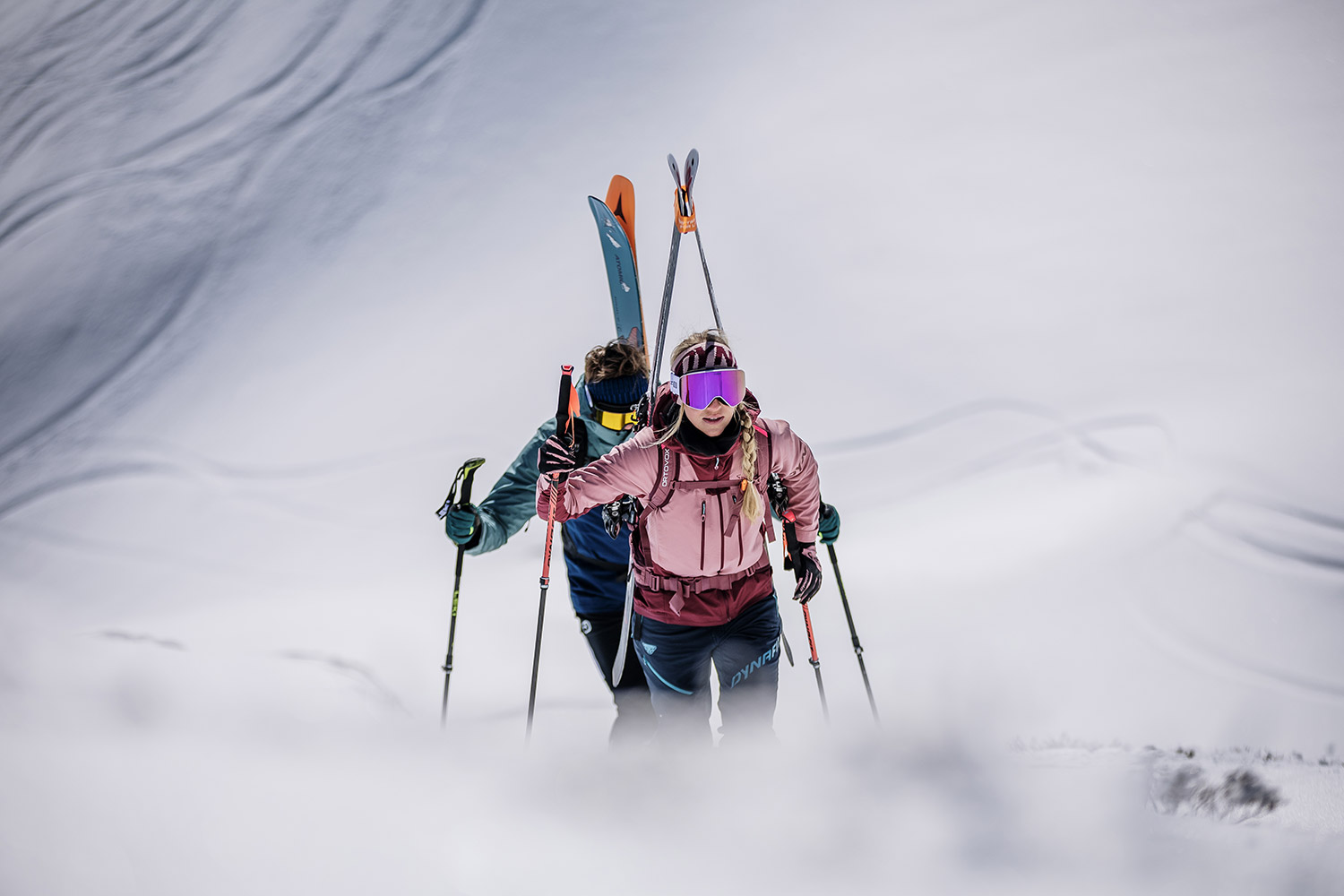 Bild Zwei Skitourengeher steigen mit den Tourenski am Rucksack einen Hang auf.