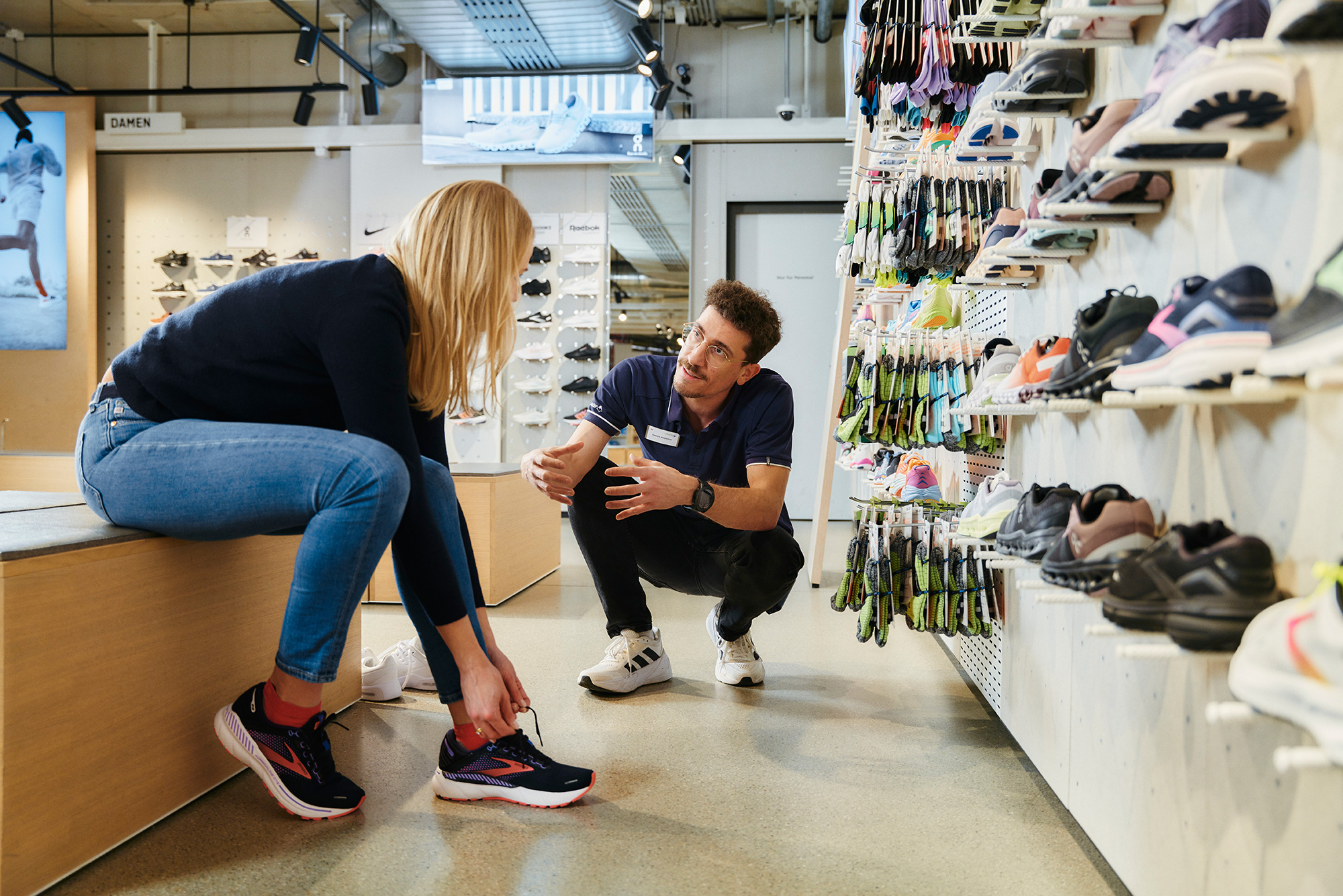 Bild Eine Kundin im Gespräch mit dem Berater. Sie probiert einen Laufschuh an.