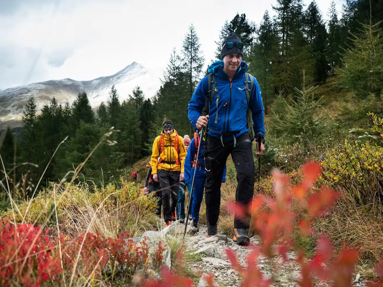 Bild Eine Gruppe Menschen wandert durch eine bunte, alpine Herbstlandschaft.