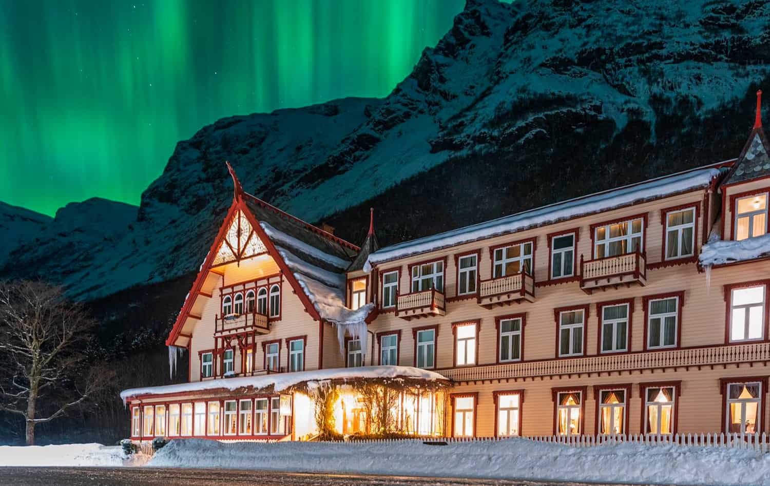 Bild Nächtliche Ansicht eines beleuchteten norwegischen Hotels, am Himmel leuchten grüne Nordlichter.
