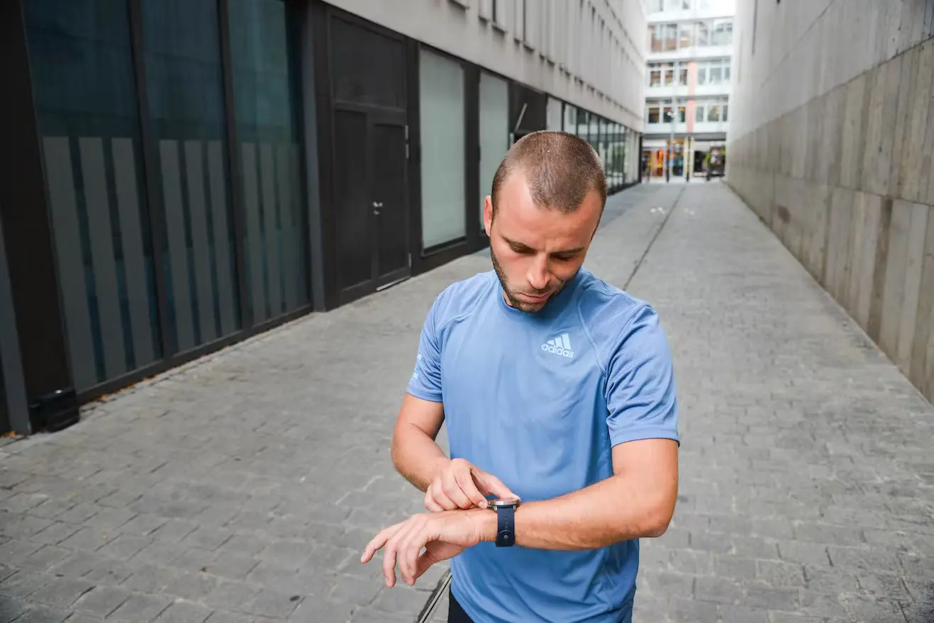 Bild Läufer steht in einer Gasse und schaut auf seine Laufuhr.