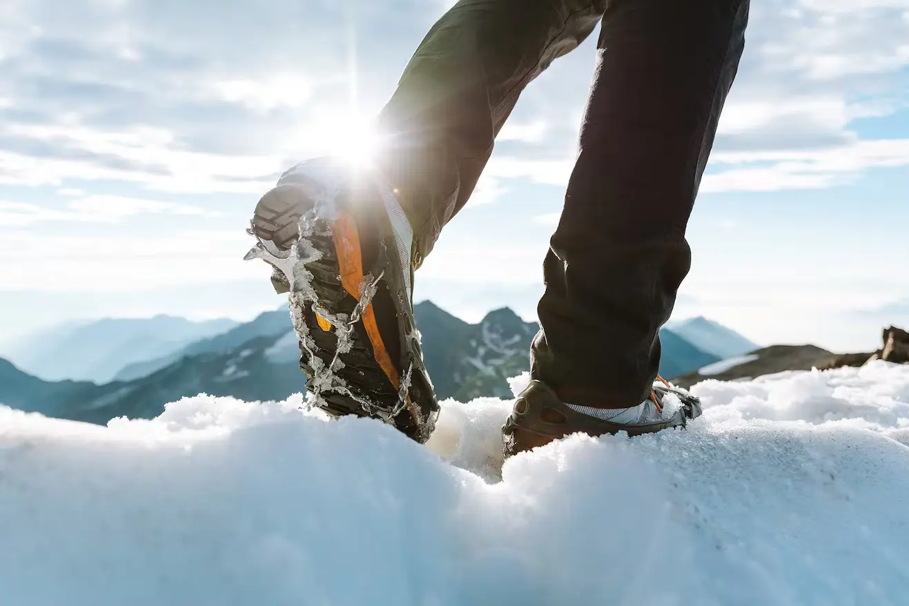 Zwei Beine, die Schuhe mit Spikes, beim Wandern im Schnee