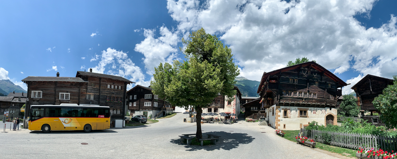 Bild Szene in Zermatt. Vor einem Gebäude steht ein gelber Postbus.
