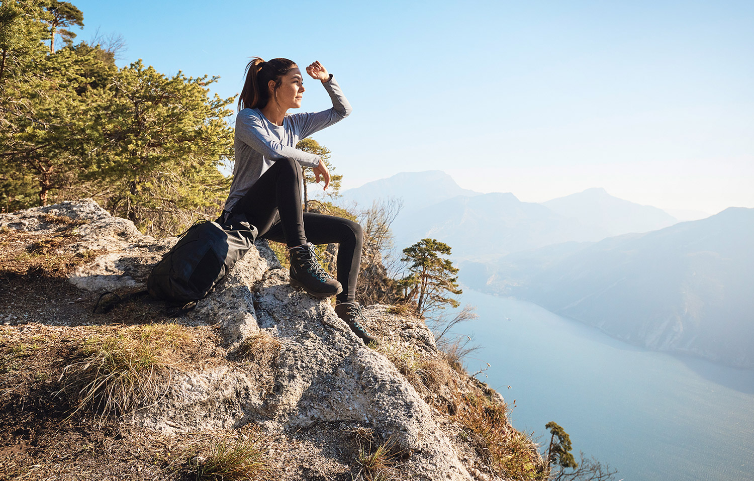 Bild Eine Frau sitzt auf einem Bergrücken in der Sonne und genießt die Aussicht über den Gardasee.