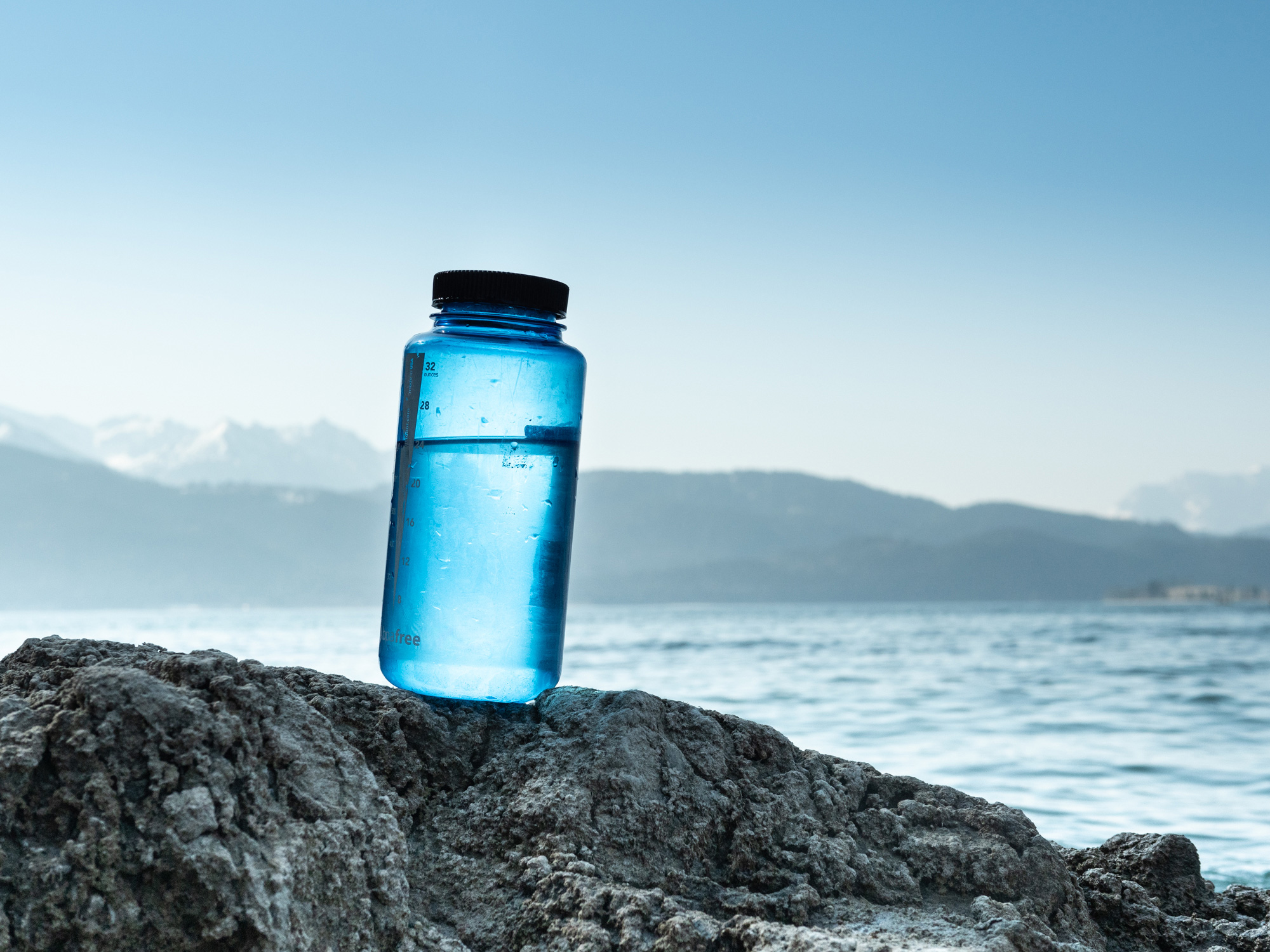 Bild Klares Wasser in einer blauen Flasche die am Seeufer steht.