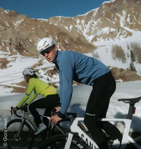Zwei Radfahrer*innen vor winterlicher Bergkulisse