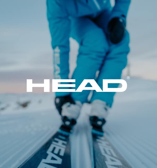 Person mit Skischuhen und Skiern und Head Logo