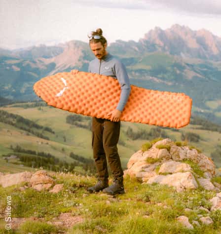 Mann trägt Isomatte in Bergpanorama