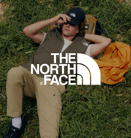 Mann liegt auf einer Wiese und The North Face Logo